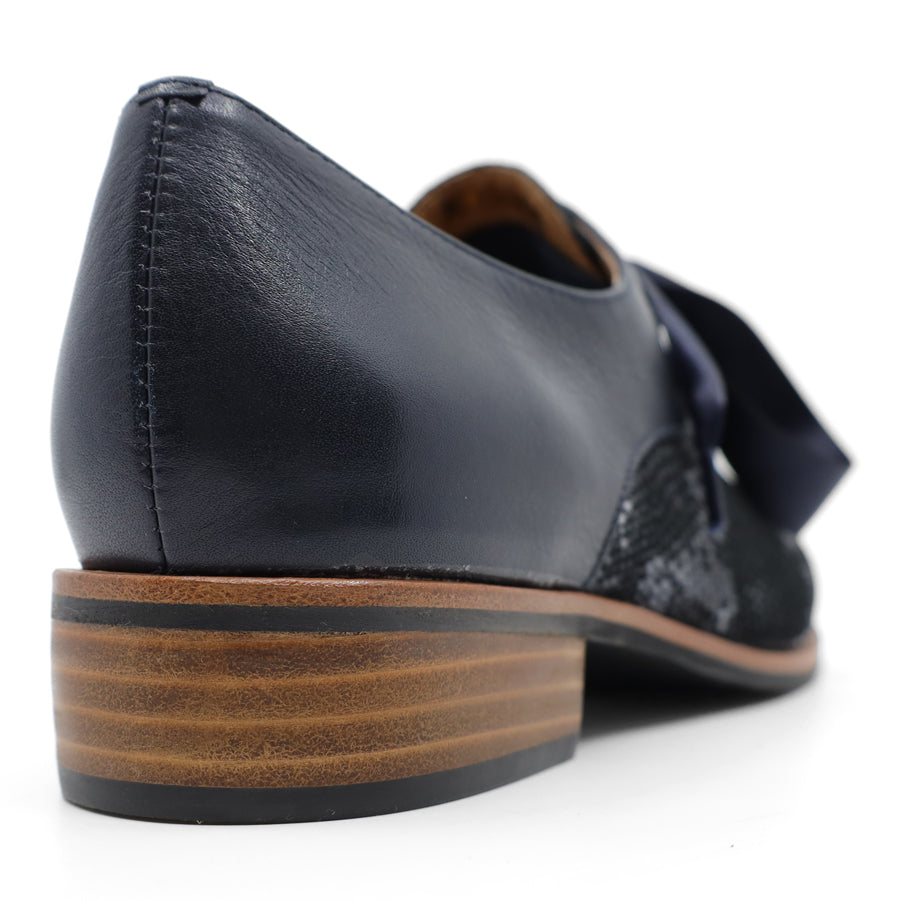 BACK VIEW OF NAVY LEATHER PATENT FLAT SHOE WITH NAVY RIBBON LACES. 